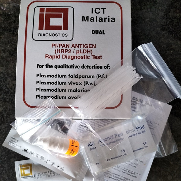 ICT Malaria Dual Test kit components including a white printed card, plastic bags, a small bottle, and alcohol pads arranged on a dark stone surface.